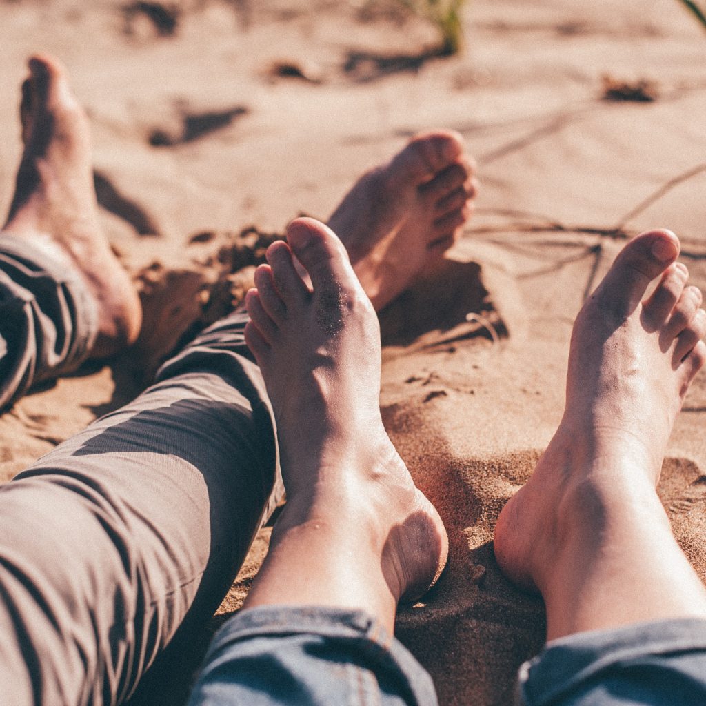 Two pairs of feet on a beach with sandy toes