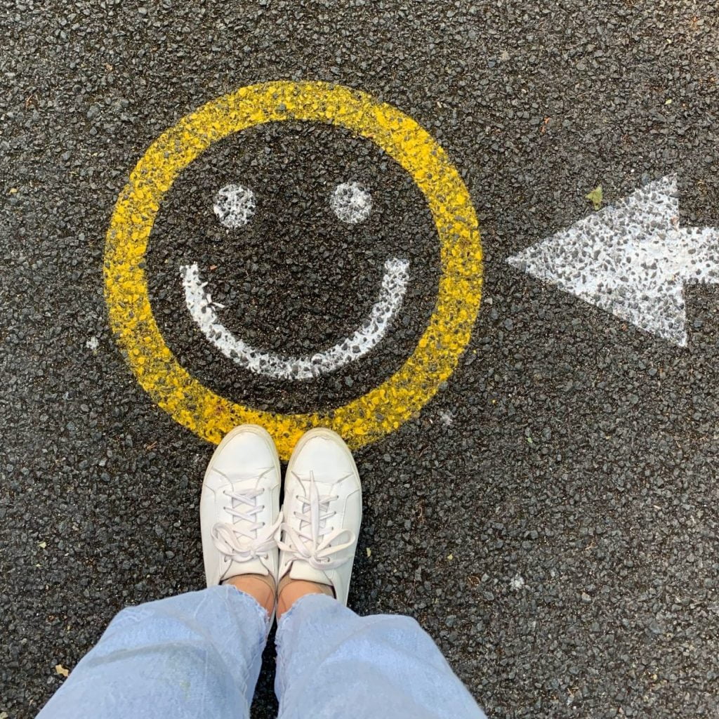 Girl standing on painted yellow smiley face with arrow pointing to the smiley face